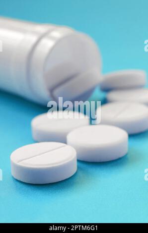 Diverse compresse bianche ricade al di fuori del vaso in plastica sulla superficie blu. Immagine di sfondo sul farmaceutico e medico, argomenti Foto Stock