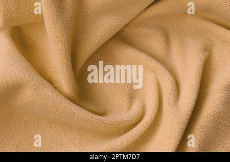 La coperta di pelliccia arancione in tessuto di pile. Uno sfondo di luce arancione peluche morbido materiale in vello con un sacco di pieghe in rilievo Foto Stock