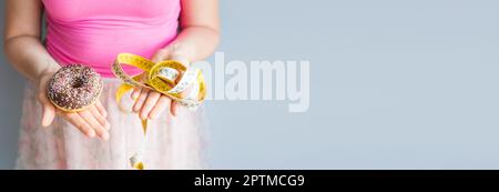 Close-up di donna di mani tenendo una ciambella e un nastro di misurazione. Il concetto di mangiare sano. La dieta Foto Stock