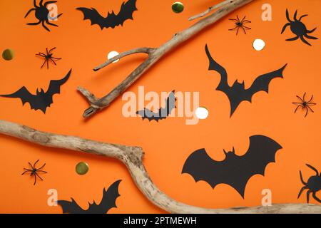 Composizione piatta con pipistrelli di carta, ragni e rami di legno su fondo arancione. Arredamento di Halloween Foto Stock