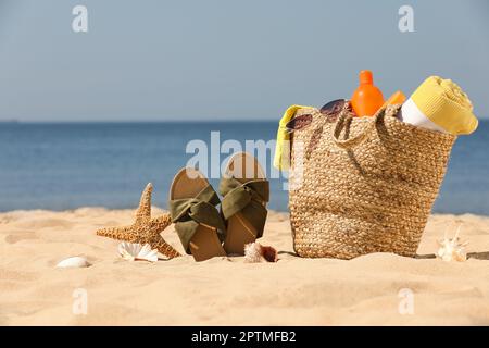 Borsa con accessori da spiaggia e ciabatte sulla sabbia vicino al mare Foto Stock