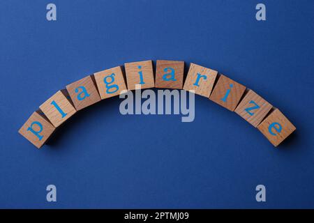 Parola plagio fatto di cubi di legno con lettere su sfondo blu, vista dall'alto Foto Stock