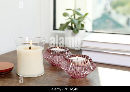 Candele che bruciano con libri e pianta della casa sul davanzale della finestra di legno Foto Stock