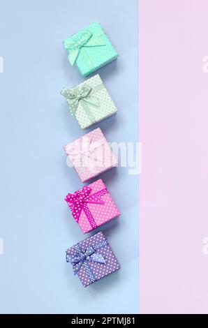 Piccole confezioni regalo di diversi colori con nastri giace su un viola e rosa colore di sfondo. Foto Stock