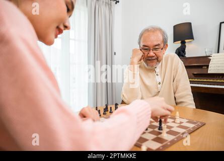 Sorridente anziano che si diverte giocando a scacchi con bella figlia a casa, infermiere caregiver in casa di cura per il tempo libero, felice attivo ritiro Foto Stock
