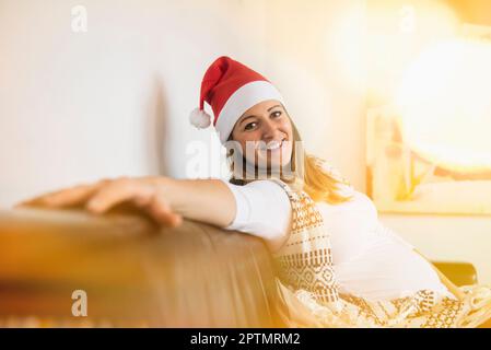 Donna incinta che indossa il cappello di Santa sul divano, Monaco, Germania Foto Stock