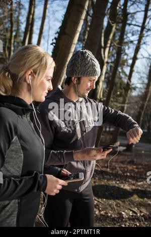 Uomo e donna in abbigliamento sportivo con smartphone con cuffie e controllo del tempo nella foresta Foto Stock