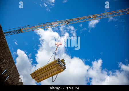 Vista ad angolo basso della gru che trasporta materiali da costruzione in un cantiere contro il cielo blu chiaro a Graz, Austria. Foto Stock