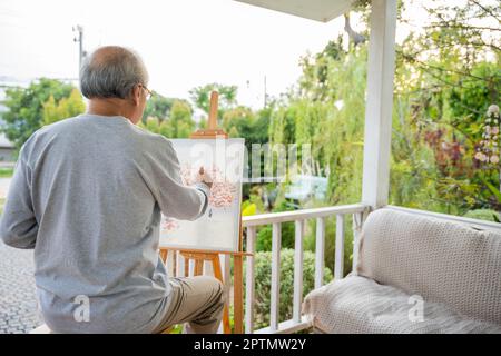 Stile di vita persone anziane sorridono dipingere al suo cavalletto fuori casa, asiatico anziano pittura immagine utilizzando pennello e olio di colore su tela, felice pensir Foto Stock