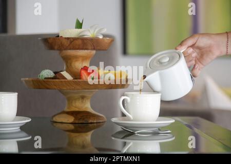 Mano di donna che tiene una teiera e che versa il tè in una tazza di ceramica bianca Foto Stock