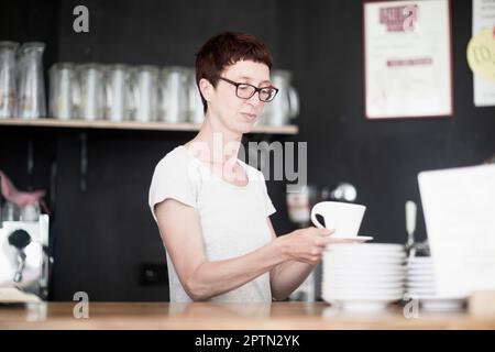 Donna matura che beve caffè nel bar di Friburgo im Breisgau, Baden-Württemberg, Germania Foto Stock