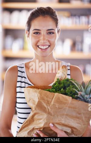 Iniziare la mia nuova dieta. Una donna attraente che tiene un sacchetto dei generi alimentari nella cucina Foto Stock