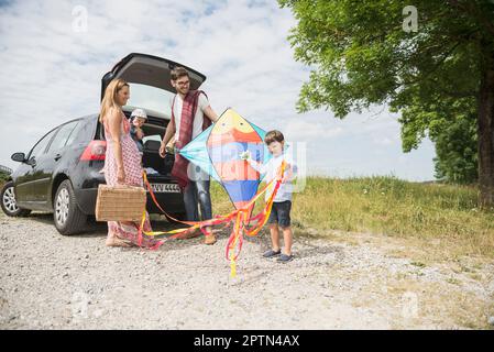 Famiglia con aquilone che scarica l'auto sul prato in campagna, Baviera, Germania Foto Stock