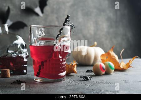 Cocktail sanguinoso di Halloween. Calice di vetro da cocktail rosso sanguinoso per Halloween e cranio a forma di bottiglia su sfondi scuri. Festa di Halloween con occhi dolci, Foto Stock