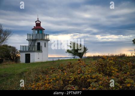 Faro, Spodsbjerg Fyr a Huntsted sulla costa della Danimarca. I raggi del sole brillano attraverso le nuvole. Prato con alberi. Foto di paesaggio dal mare Foto Stock