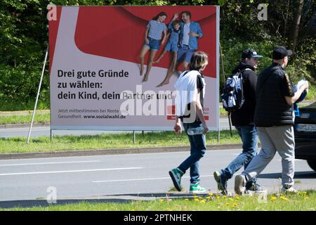 Un grande poster che chiede le elezioni sociali del 2023 il 31 maggio 2023 si trova su una strada trafficata, tre giovani stanno camminando di fronte ad essa. Si svolge ogni sei anni per tutti i prestatori di pensione, di assicurazione sanitaria e di assicurazione contro gli infortuni. Oberhausen, 27 aprile 2023 Foto Stock