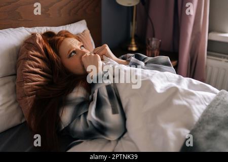 Vista laterale di una donna afflitto dal dolore che piange sdraiata da sola sul letto sotto coperta, ha depressione e stress, guardando disperatamente lontano. Foto Stock