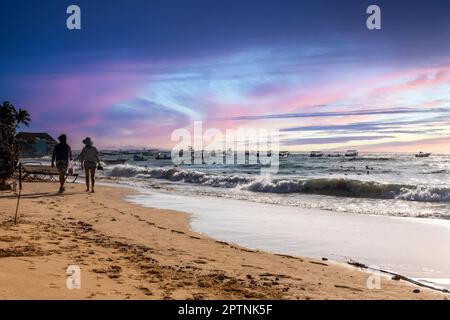 Coppia innamorata camminando lungo una bellissima spiaggia di sabbia dorata al tramonto sotto un bel cielo blu, arancione, rosa e oro. Concetto di spiaggia al tramonto. Foto Stock