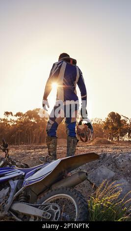 Pronto a portare tutto. Ripresa da dietro di un pilota di motocross in piedi davanti alla sua moto da corsa Foto Stock