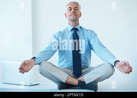 Trovare il suo centro. Scatto a tutta lunghezza di un uomo d'affari maturo seduto a gambe incrociate e meditando Foto Stock