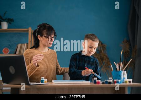 Formazione online per i bambini. Madre e figlio scolaro che guarda una video lezione sul disegno utilizzando il computer in salotto Foto Stock