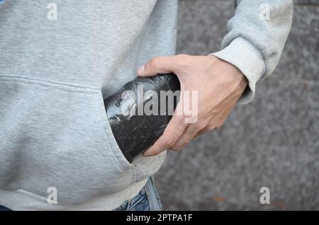 Il TRAFFICANTE DI DROGA Prendendo in borsa con cocaina al di fuori della tasca di felpa con cappuccio scuro su sfondo piastrelle close up. Il traffico di narcotici concetto. La tossicodipendenza Foto Stock