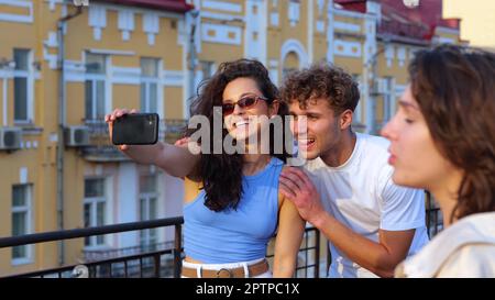 Primo piano di una giovane coppia felice, fidanzata e ragazza, che scattano foto al selfie su uno smartphone in piedi all'aperto al party sul tetto. Tramonto estivo. persone Foto Stock