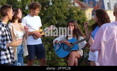 Caucasici giovani felici che suonano la chitarra divertendosi. Primo piano. Macchina fotografica avvicinandosi a musicisti maschi e femmine che suonano musica. Gli amici amano la musica Foto Stock