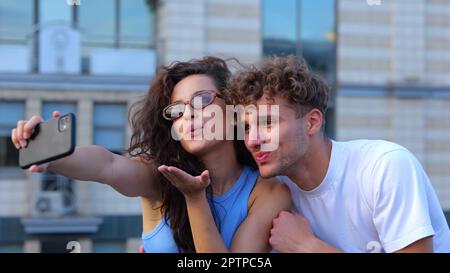 Fotocamera che si sposta indietro da felice giovane coppia ragazzo e ragazza scattando foto selfie su smartphone all'aperto al party sul tetto. Gente che festeggiano Foto Stock