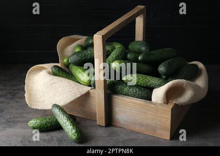 Cestino di legno pieno di cetrioli freschi maturi su tavolo grigio scuro Foto Stock