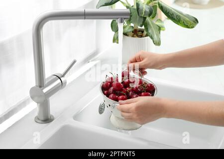 Donna lavaggio ciliegie fresche mature sotto acqua corrente in cucina, primo piano Foto Stock