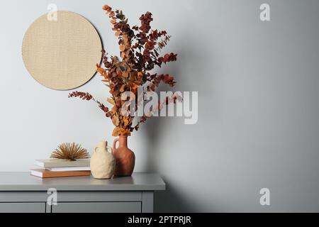 Vasi eleganti, rami di eucalipto secco e libri su tavolo grigio vicino parete bianca interni, spazio per il testo. Design degli interni Foto Stock