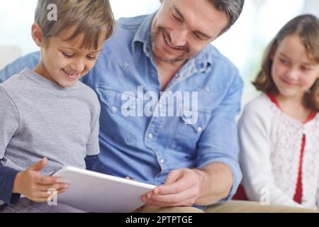 Puoi anche guardare i tuoi cartoni animati preferiti qui. un padre amorevole che usa un tablet digitale con suo figlio e sua figlia a casa. Foto Stock