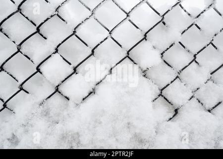 La recinzione è coperta di neve. Neve che si attacca ad una recinzione di metallo. Foto Stock