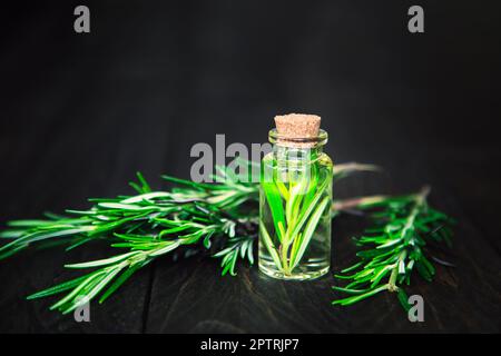 Bottiglia di vetro di olio essenziale di rosmarino con rametto di rosmarino su fondo rustico in legno. Foto Stock