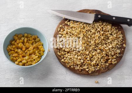 Asse di legno con noci tritate e una ciotola di uva passa, ingredienti per preparare un cupcake o una torta su uno sfondo grigio chiaro, vista dall'alto. Cucina deliziosa Foto Stock