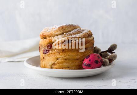 Torta di Pasqua Kraffin con noci e frutta secca, cosparsa di zucchero a velo, decorata con un uovo dipinto e rami di salice su un dorso azzurro Foto Stock