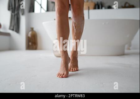 Vista in sezione bassa di piedi nudi femmina bagnati piedi schiumosi che si stoppano sul pavimento del bagno. Routine di igiene del mattino Foto Stock