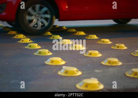 Chiodi riflettenti gialli su una strada della città, utilizzati come misura di calmamento del traffico. Foto Stock