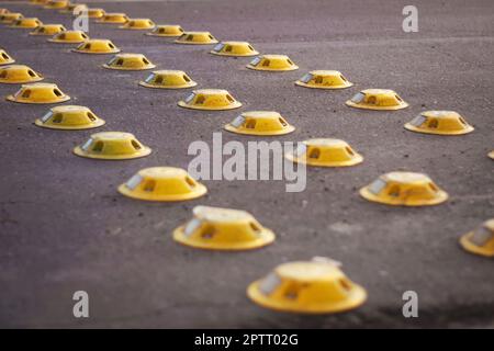 Chiodi riflettenti gialli su una strada della città, utilizzati come misura di calmamento del traffico. Foto Stock