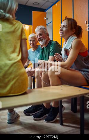 Coppia senior che parla con gli amici. Gruppo di quattro persone in palestra spogliatoio dopo l'allenamento. Concetto di vita senior. Foto Stock
