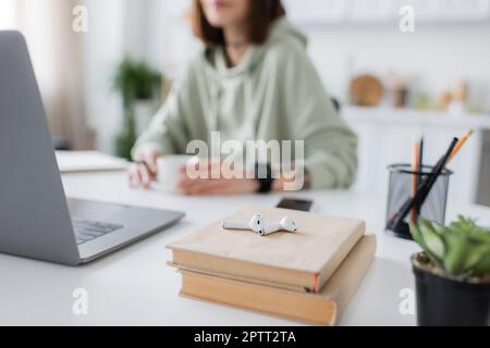 Visualizzazione ritagliata degli auricolari sui libri vicino al notebook e freelance sfocata a casa, immagine di scorta Foto Stock