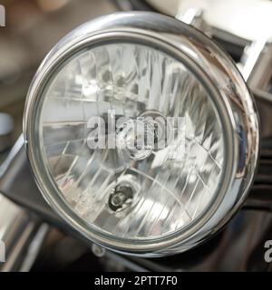 Primo piano di un faro rotondo su una moto classica. Una lampadina su una motocicletta retrò con rivestimento cromato e perfettamente mantenuta. Accessori per veicoli a motore Foto Stock