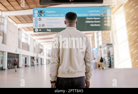 Black Black Black Vista posteriore di un uomo d'affari afro-americano che viaggia da solo e in piedi in una stazione ferroviaria mentre controlla gli orari di viaggio a bordo. Foto Stock