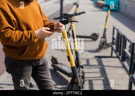 Hippster bearded utilizzando smartphone dopo aver cavalcato in scooter elettrico in città. Trasporto innovativo Foto Stock