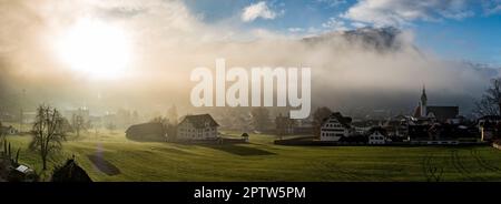 Mattina foschia o sera foschia con i raggi luminosi del sole che la penetrano nella città di Schwyz in Svizzera Foto Stock