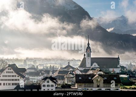 Mattina foschia o sera foschia con i raggi luminosi del sole che la penetrano nella città di Schwyz in Svizzera Foto Stock