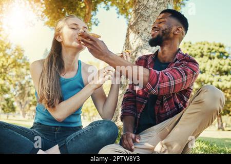 Pizza, cibo e pic-nic con una coppia diversità in un parco durante l'estate per un appuntamento romantico insieme. Fast food, mangiare e l'amore con un uomo e una donna d Foto Stock