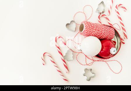 Le caramelle di Natale, insieme ai taglierini dei biscotti, ai giocattoli dell'albero di Natale ed al filo rosso per il rivestimento del regalo, si trovano su un tavolo bianco. Messa a fuoco selettiva, rumore. CHRI Foto Stock