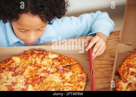 La pizza hawaiana è la migliore. Un ragazzo carino che guarda la pizza davanti a lui Foto Stock